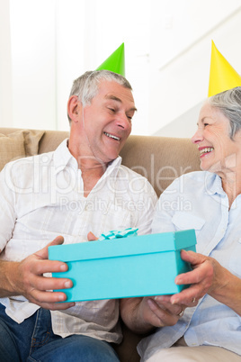 Senior couple sitting on couch wearing party hats holding a gift