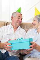 Senior couple sitting on couch wearing party hats holding a gift