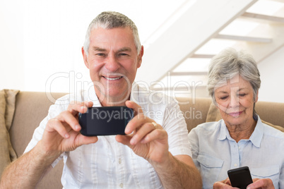 Senior couple sitting on couch using their smartphones