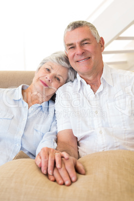 Retired couple holding hands on couch smiling at camera