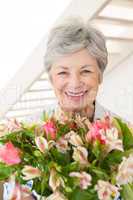 Retired woman holding bouquet of flowers smiling at camera