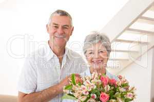Senior couple smiling at camera holding bouquet of flowers