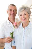 Senior man offering a rose to his partner smiling at camera