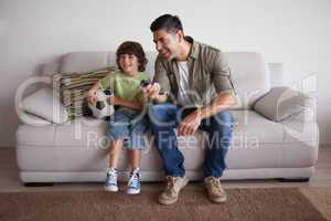 Father and son with football watching tv in the living room