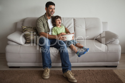 Father and son with popcorn bowl watching tv in the living room