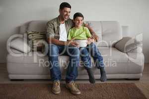 Father and son with popcorn bowl watching tv in living room