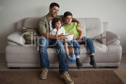 Father and sons with popcorn bowl watching tv in the living room