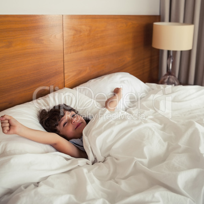 Young boy stretching arms in bed