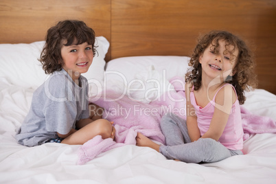 Portrait of happy siblings sitting in bed