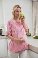 Pregnant woman holding apple in kitchen