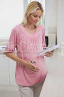 Pregnant woman looking at book in kitchen