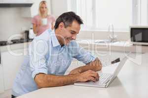 Man using laptop while woman drinking coffee in kitchen