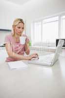 Woman using laptop while drinking coffee in kitchen