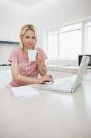 Woman using laptop while drinking coffee in kitchen