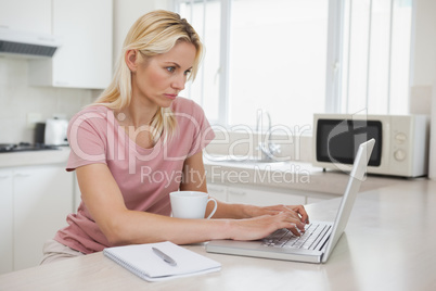 Side view of a serious woman using laptop in kitchen