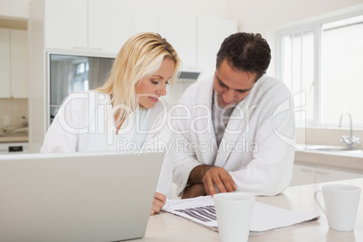 Casual business couple with laptop looking at graphs in kitchen