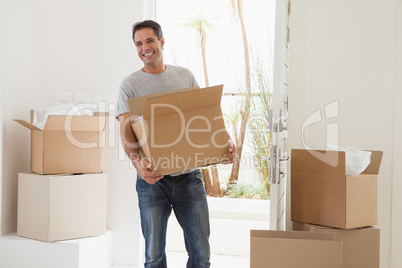 Smiling man carrying boxes in new house