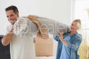 Couple carrying rolled rug after moving in a house