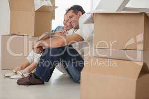 Smiling couple sitting amid boxes in new house