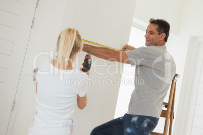 Woman holding drill while man measuring wall