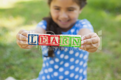 Happy girl holding block alphabets as 'learn' at park