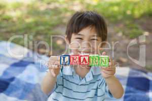 Happy boy holding block alphabets as 'learn' at park