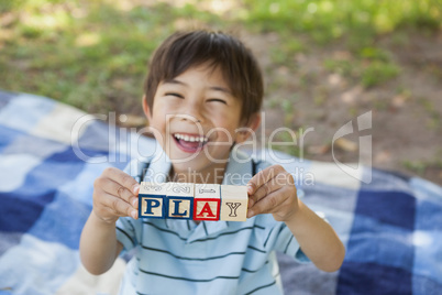 Happy boy holding block alphabets as 'play' at park