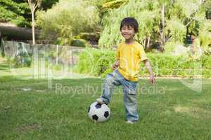 Cute little boy with football standing at park