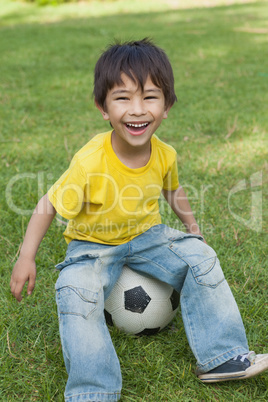 Cute little boy sitting on football at park