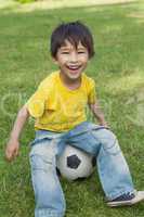 Cute little boy sitting on football at park