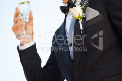 Mid section of flowers on lapel of male as he holds champagne gl