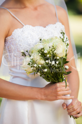 Mid section of a beautiful bride with bouquet in park