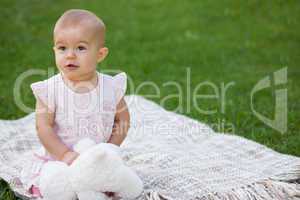 Baby with stuffed toy sitting on blanket at park