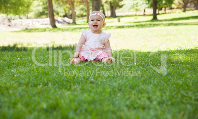 Cheerful cute baby sitting on grass at park