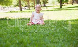 Cheerful cute baby sitting on grass at park