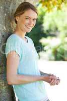 Happy woman leaning against tree at park