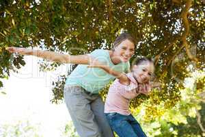 Portrait of mother and daughter with arms outstretched at park