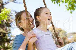 Happy mother swinging daughter at park
