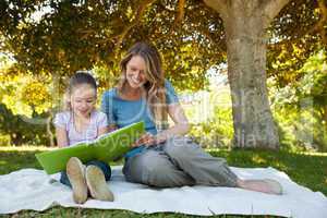 Happy mother and daughter reading a book at park