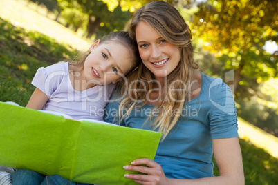 Happy mother and daughter reading a book at park