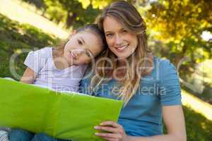 Happy mother and daughter reading a book at park