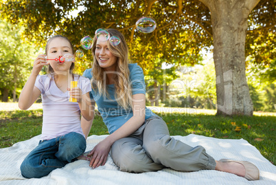 Mother with her daughter blowing soap bubbles at park