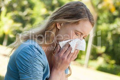 Woman blowing nose with tissue paper at park