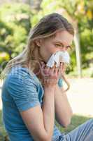 Woman blowing nose with tissue paper at park