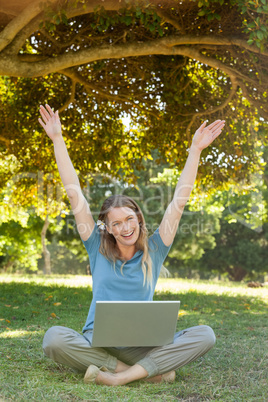 Cheerful woman with laptop raising hands at park