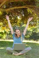 Cheerful woman with laptop raising hands at park