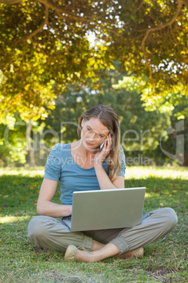 Relaxed woman using laptop and mobile phone at park