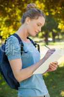 Beautiful young woman writing on clipboard at park