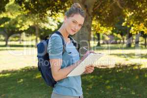 Beautiful young woman writing on clipboard at park