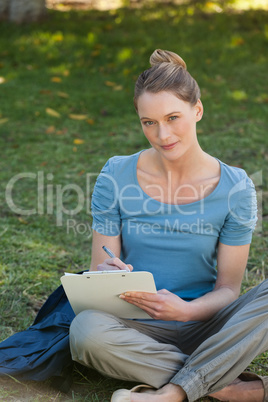 Relaxed young woman writing on clipboard at park